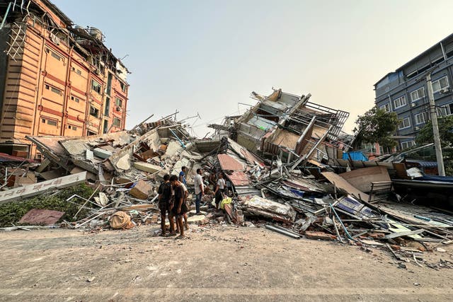 <p>People stand near debris of a collapsed building following an earthquake in Mandalay, Myanmar, on 28 March 2025</p>