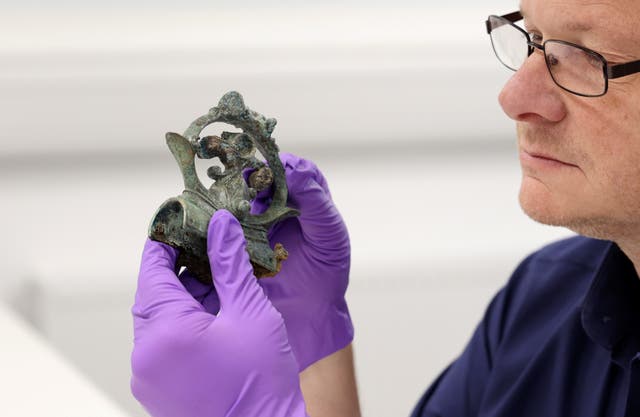 <p>Professor Tom Moore, head of archaeology at Durham University, holds a decorative copper alloy finial from a huge Iron Age hoard discovered in a Yorkshire field</p>